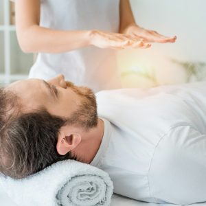 bearded man lying on massage table and receiving reiki treatment