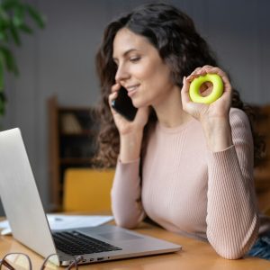 Businesswoman sit at workplace desk using expander to relief hand wrist pain from long laptop usage