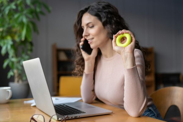 Businesswoman sit at workplace desk using expander to relief hand wrist pain from long laptop usage