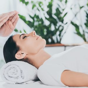 cropped shot of calm young woman with closed eyes receiving reiki treatment