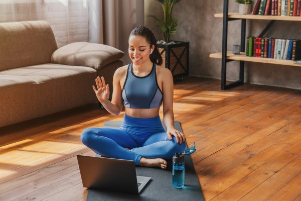 Sport training online. Young woman sits on the floor and talking with coach by laptop