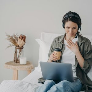 Woman life coach in headset conducts online consultation by video call on laptop in bedroom at home